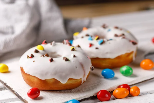 Concepto de cocina, horneado y comida - primer plano. Dos rosquillas en esmalte blanco con dragee de color chocolate en un tablero decorativo sobre un fondo oscuro . —  Fotos de Stock