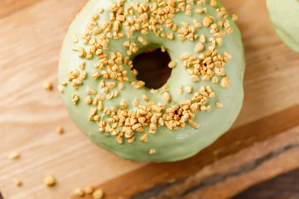Concept of cooking, baking and food - close-up. Donut with pistachio glaze and nut sprinkling on a decorative board. Trend colors.