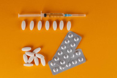 Turuncu bir arka plan üzerinde beyaz oval şekilli tabletler ve tıbbi bir şırınga saçılması.