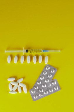 Beyaz oval şekilli tabletler ve sarı bir arka plan üzerinde tıbbi bir şırınga bir saçılma.