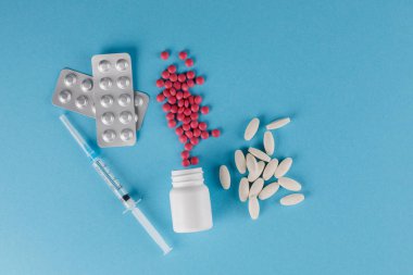 Ambalaj hapları ve tıbbi şırınga. Tabletlerin saçılması. Mavi bir arka plan üzerinde bir kavanoz dan dökülen haplar.