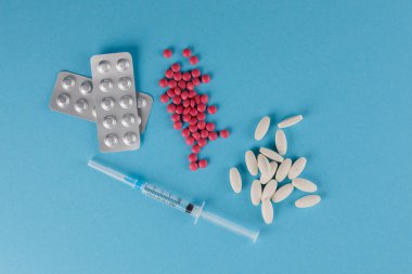 Ambalaj hapları ve tıbbi şırınga. Mavi arka planda hap saçılması.