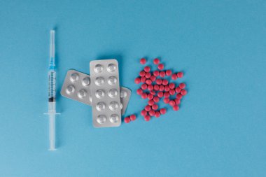 Ambalaj hapları ve tıbbi şırınga. Mavi arka planda hap saçılması.