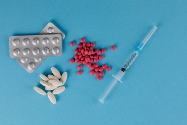 Ambalaj hapları ve tıbbi şırınga. Mavi arka planda hap saçılması.