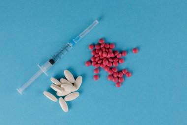 Ambalaj hapları ve tıbbi şırınga. Mavi arka planda hap saçılması.