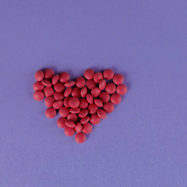 보라색 배경에 심장의 형태로 빨간 알약의 산란. 사각형. — 스톡 사진