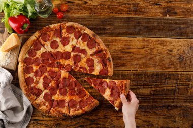 Tahta bir masada Pepperoni pizzası. El ve malzemelerle natürmort. Üstte görüntü.