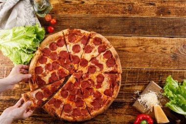 Tahta bir masada Pepperoni pizzası. Elleri ve malzemeleri ile natürmort. Kopyalama alanı.
