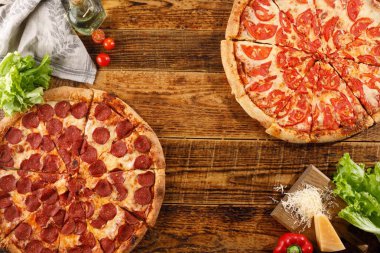 Pizza Pepperoni ve Margarita tahta bir masada. Malzemelerle natürmort.