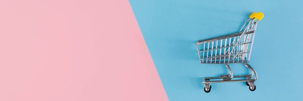 Shopaholiskt. Köpare. Köpkoncept. Närbild. En isolerad vagn och kundvagn på en rosa och blå bakgrund bisected. Uppfattat utrymme. Banderoll. — Stockfoto
