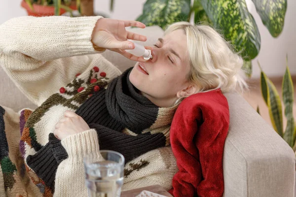 La chica del suéter está enferma acostada en el sofá. Resfriados y gripe. El paciente contrajo un resfriado, se siente enfermo y usa gotas para la nariz. Chica malsana . —  Fotos de Stock