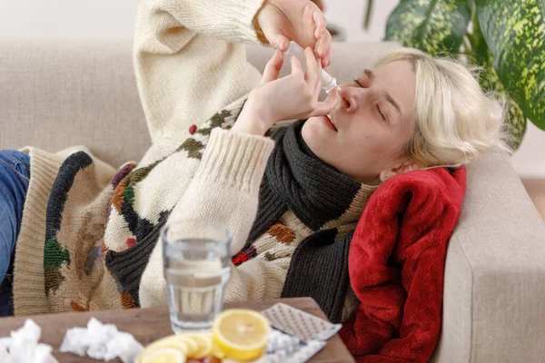 Дівчинка в светрі хвора лежить на дивані. Застуда і грип. Пацієнт застудився, захворів і використовує краплі для носа. Нездорові дівчата . — стокове фото