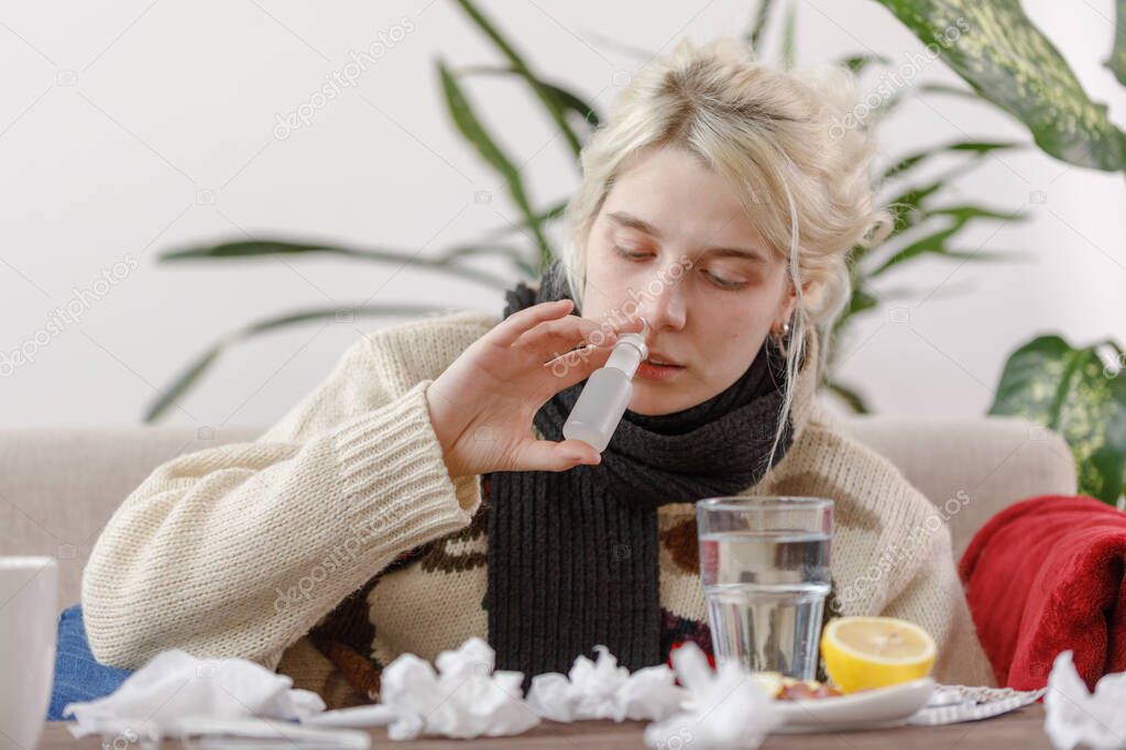 The girl in the sweater is sick lying on the couch. Colds and flu. The patient caught a cold, feeling sick and uses drops for the nose. Unhealthy girl.