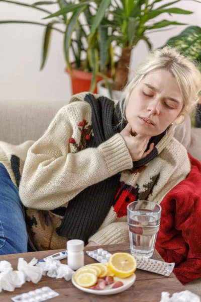 A lány a pulóverben rosszul van a kanapén fekve. Megfázás és influenza. A beteg megfázott, rosszul lett és torokgyulladása volt. Egészségtelen lány torokfájással. — Stock Fotó