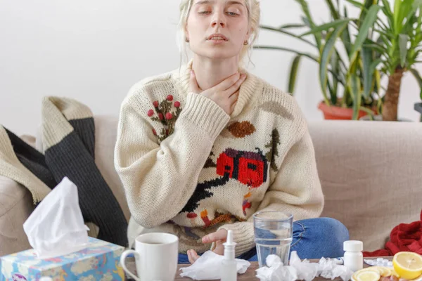 La chica del suéter está enferma, sentada en el sofá. Resfriados y gripe. El paciente contrajo un resfriado, sintiéndose enfermo y dolor de garganta. Chica malsana con dolor de garganta . —  Fotos de Stock