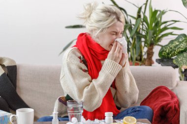 Kanepede oturan süveterli bir kız hapşırır. Hasta hasta hasta hasta oldu, hasta ve kağıt peçeteye hapşırıyor. Sağlıksız bir kız burnunu sildi..