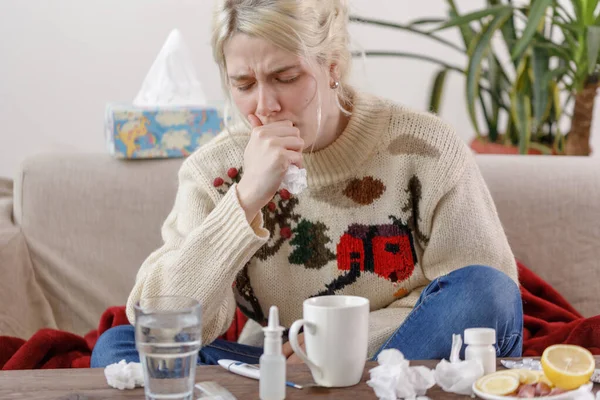 Das Mädchen im Pullover hustet, auf der Couch sitzend. Erkältungen und Grippe. der Patient erkältete sich, fühlte sich krank und hustete in einer Serviette. ein ungesundes Mädchen hustet. — Stockfoto