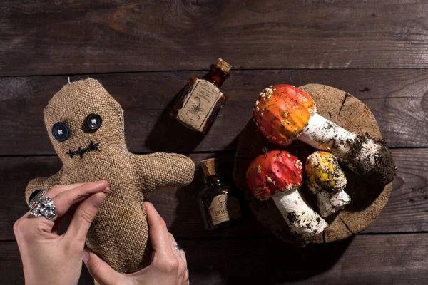 Voodoo doll on a wooden background with dramatic lighting. A sacking doll on a wooden background and bottles with a poisonous substance and amanita mushrooms. Pierce with a club.
