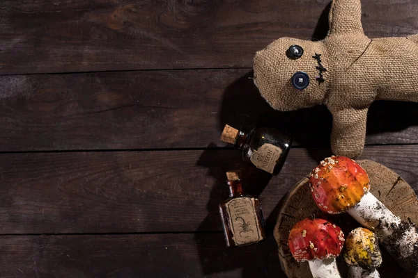 Voodoo doll on a wooden background with dramatic lighting. A sacking doll on a wooden background and bottles with a poisonous substance and amanita mushrooms. Pierce with a club.