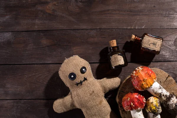 Voodoo doll on a wooden background with dramatic lighting. A sacking doll on a wooden background and bottles with a poisonous substance and amanita mushrooms. Pierce with a club.