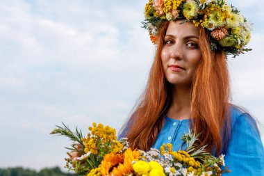 Kafasında çiçek çelengi ve bir buket kır çiçeğiyle Slav güzelliği. Antik putperest kökenli kutlama konsepti. Yaz gündönümü günü. Yaz ortası.