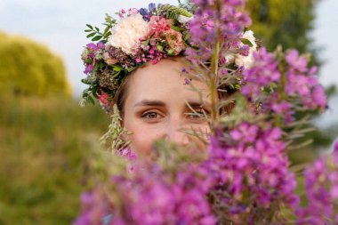 Kafasında çiçek çelengi ve bir buket kır çiçeğiyle Slav güzelliği. Antik putperest kökenli kutlama konsepti. Yaz gündönümü günü. Yaz ortası.
