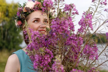 Kafasında çiçek çelengi ve bir buket kır çiçeğiyle Slav güzelliği. Antik putperest kökenli kutlama konsepti. Yaz gündönümü günü. Yaz ortası.