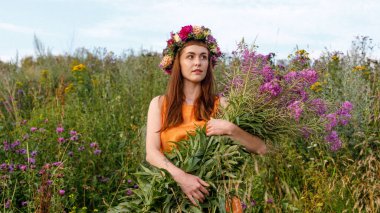 Kafasında çiçek çelengi ve bir buket kır çiçeğiyle Slav güzelliği. Antik putperest kökenli kutlama konsepti. Yaz gündönümü günü. Yaz ortası.