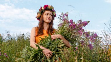 Kafasında çiçek çelengi ve bir buket kır çiçeğiyle Slav güzelliği. Antik putperest kökenli kutlama konsepti. Yaz gündönümü günü. Yaz ortası.