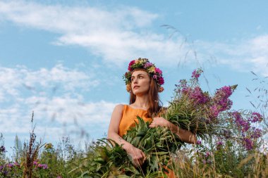 Kafasında çiçek çelengi ve bir buket kır çiçeğiyle Slav güzelliği. Antik putperest kökenli kutlama konsepti. Yaz gündönümü günü. Yaz ortası.