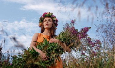 Kafasında çiçek çelengi ve bir buket kır çiçeğiyle Slav güzelliği. Antik putperest kökenli kutlama konsepti. Yaz gündönümü günü. Yaz ortası.