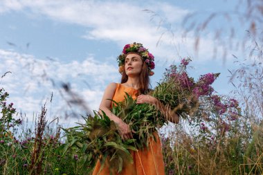 Kafasında çiçek çelengi ve bir buket kır çiçeğiyle Slav güzelliği. Antik putperest kökenli kutlama konsepti. Yaz gündönümü günü. Yaz ortası.