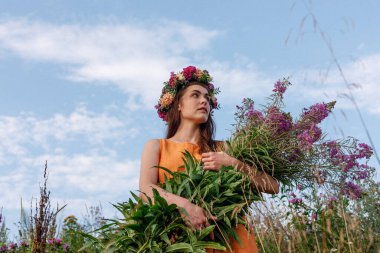 Kafasında çiçek çelengi ve bir buket kır çiçeğiyle Slav güzelliği. Antik putperest kökenli kutlama konsepti. Yaz gündönümü günü. Yaz ortası.