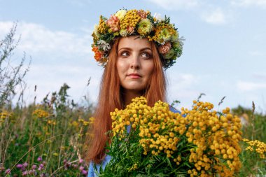 Kafasında çiçek çelengi ve bir buket kır çiçeğiyle Slav güzelliği. Antik putperest kökenli kutlama konsepti. Yaz gündönümü günü. Yaz ortası.