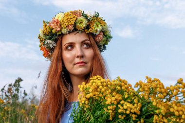 Kafasında çiçek çelengi ve bir buket kır çiçeğiyle Slav güzelliği. Antik putperest kökenli kutlama konsepti. Yaz gündönümü günü. Yaz ortası.