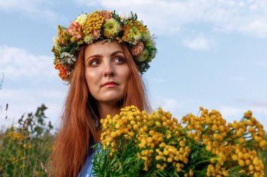 Kafasında çiçek çelengi ve bir buket kır çiçeğiyle Slav güzelliği. Antik putperest kökenli kutlama konsepti. Yaz gündönümü günü. Yaz ortası.