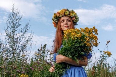 Kafasında çiçek çelengi ve bir buket kır çiçeğiyle Slav güzelliği. Antik putperest kökenli kutlama konsepti. Yaz gündönümü günü. Yaz ortası.