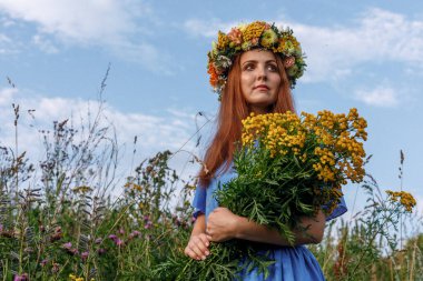 Kafasında çiçek çelengi ve bir buket kır çiçeğiyle Slav güzelliği. Antik putperest kökenli kutlama konsepti. Yaz gündönümü günü. Yaz ortası.