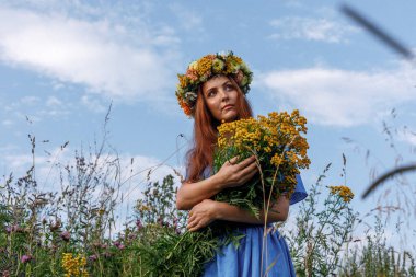 Kafasında çiçek çelengi ve bir buket kır çiçeğiyle Slav güzelliği. Antik putperest kökenli kutlama konsepti. Yaz gündönümü günü. Yaz ortası.