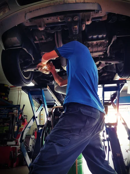 Car service, repair & maintenance. Professional car mechanic man working under lifted car in auto repair service.