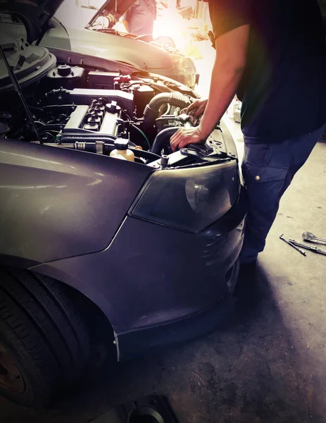 Car service, repair & maintenance. Professional car mechanic man working under lifted car in auto repair service.