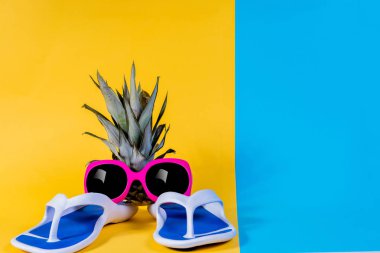 Mavi parmak arası terlik, sandalet, güneş gözlüğü ve ananas. Yaz önümüzdeki kavramdır. En az style, minimalist fotoğraf. Pastel renkler sarı, pembe ve mavi arka plan.