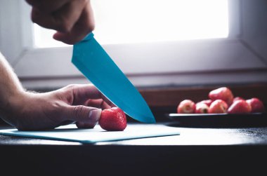 Kesme ve çilek hazırlanıyor. Adam meyve, kırmızı taze çilek kesiyor.