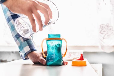 Bebek için hazırlık süt. Baba süt çocuğu için hazırlar. Baba rolü. Kavramı bir yaşam tarzı. Adam su bir şişe süt ile içine dökülen. Bir çocuk için yapay süt.