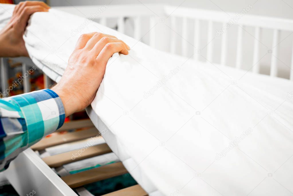 Construction of bed for children. Man arranges a mattress on a cot for a child. Role of the father in child's life. Father folds bed for a newborn child, growing up children, Concept of parenthood.