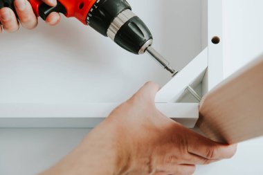 Kendinden montajlı mobilya. Adam ahşap bir mobilya parçası toplanır. Bunu kendiniz evde, DIY. Adam bir kablosuz kullanarak ahşap öğelerini birleştirir. Tesisatçısı çalışma.