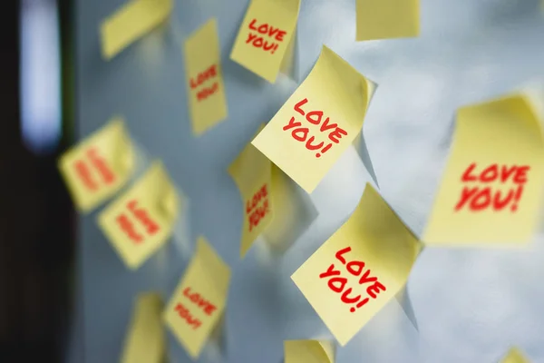 A lot of Yellow stickers inscription Love You on the white fridge. Yellow note on fridge. Concept of reminder, alarm. Leaving a message to a loved one, expressing love.