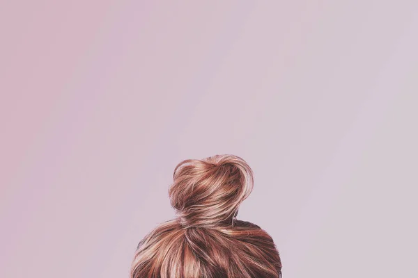 A view of the back of a woman's head. Hair wrapped in a bun on a light pink pastel background. Content completion concept.