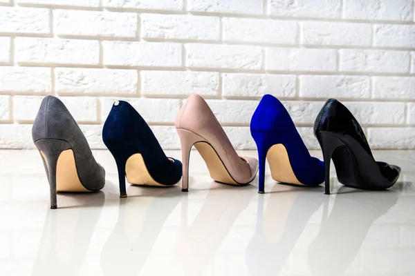 Different colors of high heels white background, brick wall. Perfect high heels footwear, gray, navy blue, beige, blue, black. Matt and shiny high heels. Fashion and beauty. Female shoes.