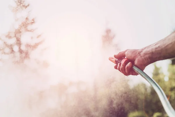 Watering plants in the garden, irrigating the soil. Garden work. The man is watering plants in the garden. A view of a man holding a coat. Saving water, care of plants.